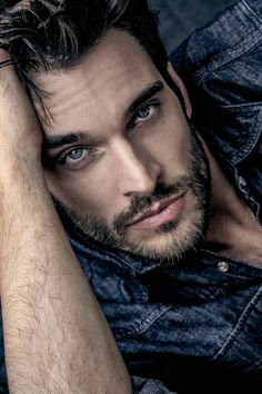 a close up of a person wearing a denim shirt and holding his hand on his head