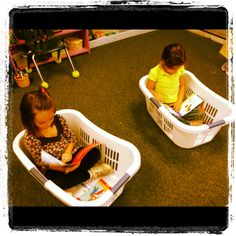 two children sitting in plastic baskets on the floor with toys and books written below them