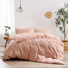 a bed with pink sheets and pillows in a white room next to a potted plant