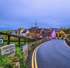 the road is lined with colorful houses on either side and there are signs pointing in different directions