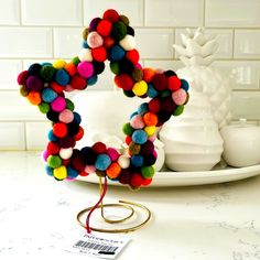 a wreath made out of pom - poms sits on a counter next to a pineapple