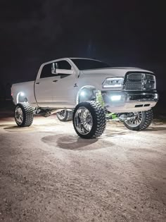 a white truck parked on top of a dirt road at night with its lights on