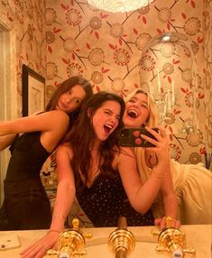 three women taking a selfie in front of a mirror with gold faucets