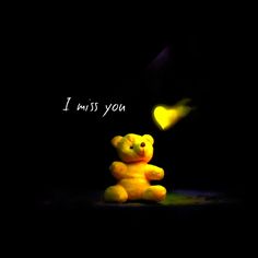 a yellow teddy bear sitting in the dark with a message below it that says i miss you