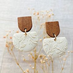 two white earrings with wood accents hanging from hooks on a planter next to some dried flowers