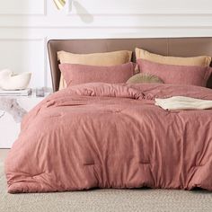 a bed with pink sheets and pillows on top of it in a white room next to a lamp