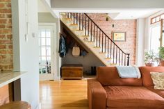 a living room filled with furniture and a stair case in front of a brick wall