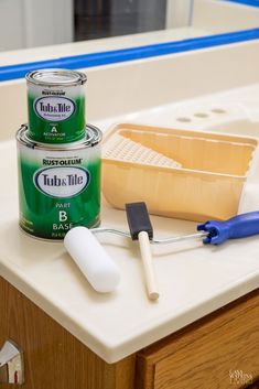 two cans of paint sitting on top of a counter next to a brush and spatula