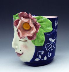 a ceramic vase with a flower on it's head and leaves around the face