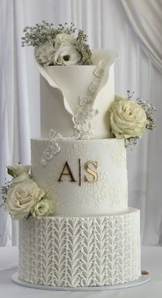 a three tiered wedding cake with white flowers on the top and initials on the side