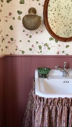 a bathroom sink under a mirror next to a wall paper with flowers and leaves on it