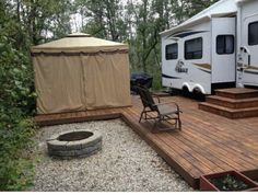 a camper trailer is parked next to a deck with a chair and fire pit