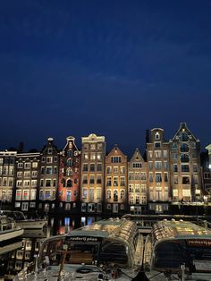 several boats are docked in front of some buildings at night, with the lights on