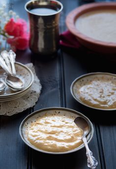 two bowls of food on a table with silver spoons and flowers in the background