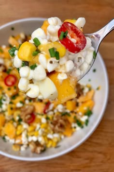 a spoon full of food on top of a white plate next to a wooden table