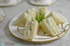 several small sandwiches on a plate with green garnish and gold trim around the edges