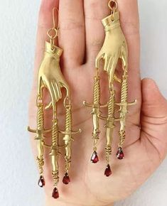 From these golden drop earrings dangle dainty hands, and in those dainty hands are knives, and from those knives drips blood. The faceted red glass gems glimmer dramatically in candle light and are real attention grabbers. AVENGE set are approx 8cm long. TINY VENGEANCE are approx 6cm long. Dagger Earrings, Gothic Earrings, Hanging Jewelry, Party Earrings, Cross Earrings, Red Stone, Tassel Earrings, Cute Jewelry, Kitsch