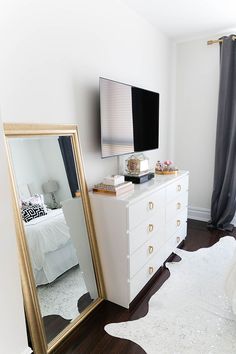 a white dresser with a mirror and a large gold framed tv on top of it