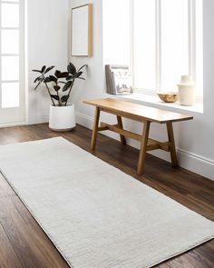 a white rug with a wooden table in the middle and potted plant next to it