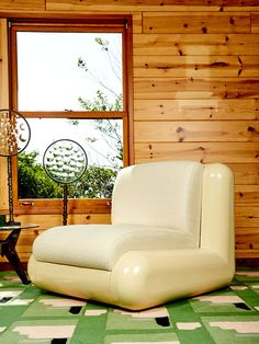 a white chair sitting in front of a window next to a green and white rug