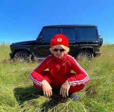 a woman sitting in the grass next to a black jeep