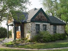 a small brick house sitting in the middle of a lush green field