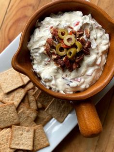 a wooden bowl filled with dip surrounded by crackers