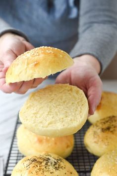 a person holding a piece of bread in front of several buns on a cooling rack