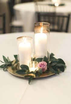 three candles are sitting on a gold plate with greenery and pink roses in the center