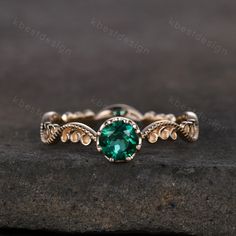 a green stone ring sitting on top of a piece of rock with gold accents and beading around the band