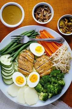 a white plate topped with meat, veggies and hard boiled eggs