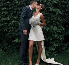 a man and woman kissing in front of some bushes