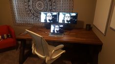 two laptops sitting on top of a wooden desk in front of a wall hanging