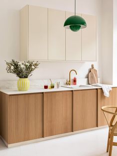 a kitchen with white counter tops and wooden cabinetry next to a green light hanging over the sink