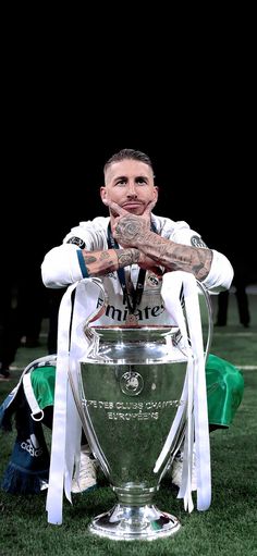 a man sitting on top of a soccer field next to a large trophy in front of him