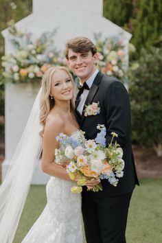 a bride and groom pose for a photo in front of a floral arch at their wedding