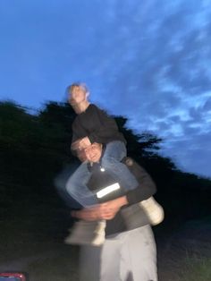 a man carrying another man on his back in the night sky with trees and clouds behind him