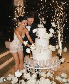 a newly married couple cutting their wedding cake with sparklers in the air behind them