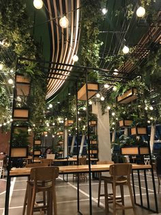 the interior of a restaurant with tables and stools covered in greenery, hanging from the ceiling