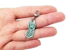 a hand holding a green and white keychain with an 8 - bit figure on it