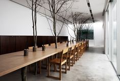 a long wooden table with chairs and vases on it in front of a large window