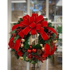 a christmas wreath with red bows and ornaments hanging on a window sill in front of a glass door