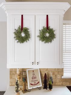 two wreaths are hanging on the wall above a kitchen counter with other christmas decorations