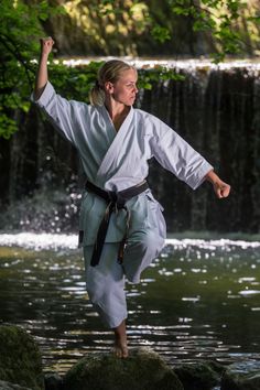 a woman standing on top of a rock in front of a waterfall wearing a kimono