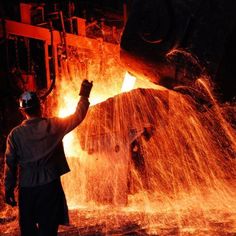 a man standing in front of a large piece of metal with fire coming out of it