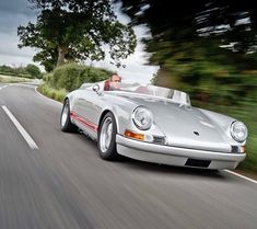 a silver sports car is driving down the road with trees in the backgroud