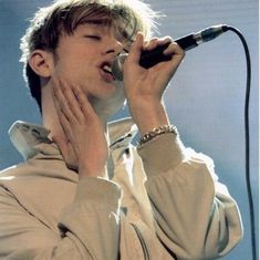 a young man singing into a microphone while holding his hands up to his mouth with both hands