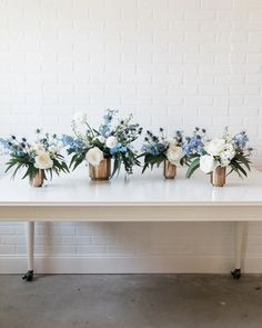 three vases with flowers are sitting on a white table in front of a brick wall