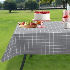 a table topped with a cake next to a basket of fruit on top of a green field