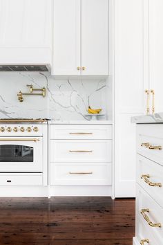 a white kitchen with marble counter tops and gold pulls on the oven door knobs